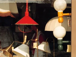 Blick ins Schaufenster von Lampen Krömer: rote Pendelleuchte, Messing-Stehleuchte und Kugelleuchten mit Preisschildern